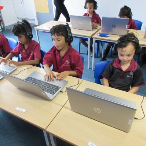 Each child wearing a headset using the laptop in front of them
