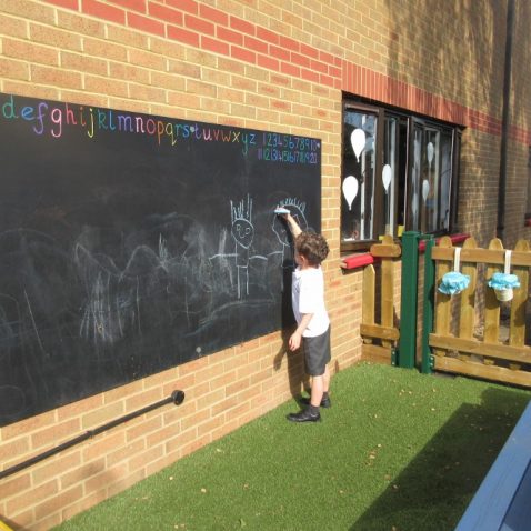 little boy drawing on outdoor chalk board