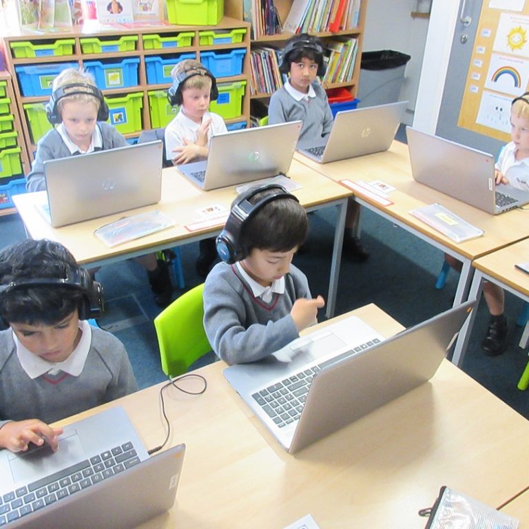 group of young children using laptops with headphones on