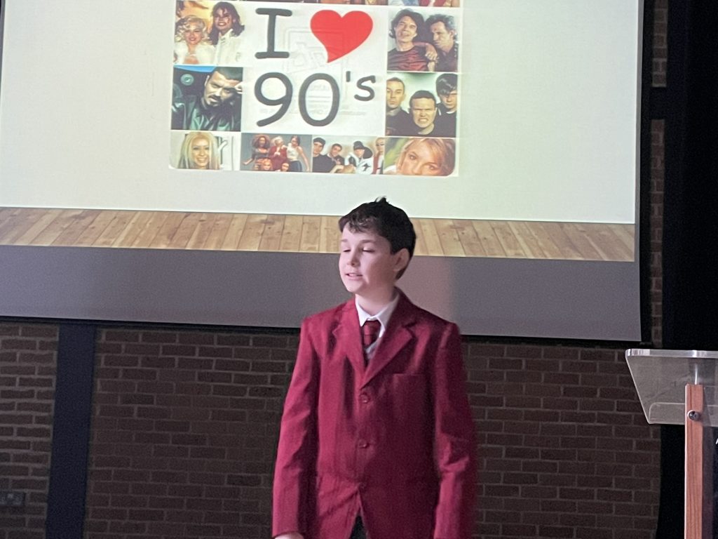 student talking on a stage, with a presentation in the background called "I love the 90's"