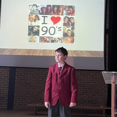 student talking on a stage, with a presentation in the background called "I love the 90's"