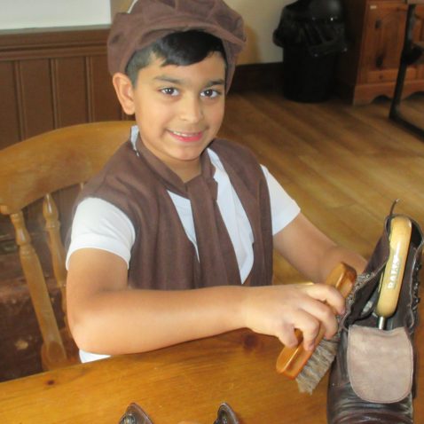 student in period clothes shining a pair of shoes