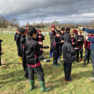 students and teachers out on a field looking at their wooden tools