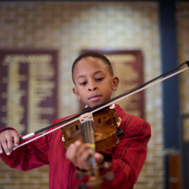 Boy in The Mall School uniform is in the Theatre playing a violin