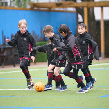 Schoolboys in PE kit playing football on outdoor playground