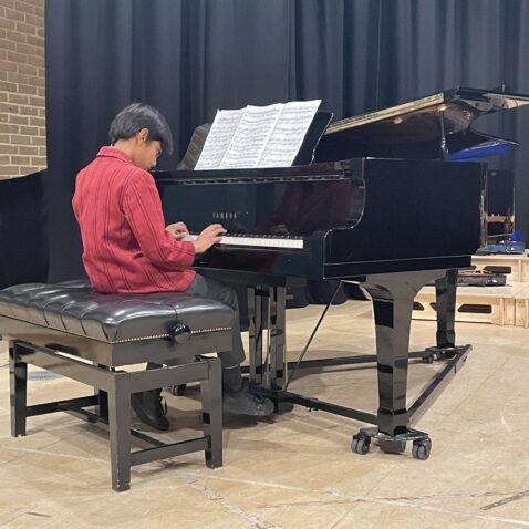 Schoolboy in maroon Mall School blazer is playing a large black piano