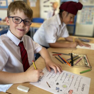 Schoolboy in classroom, writing a poem at his desk