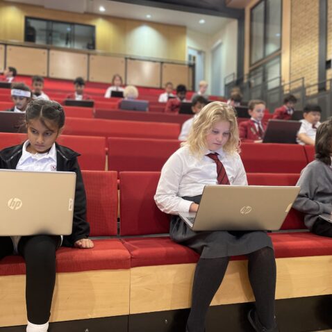 Pupils sitting in The Mall Theatre, using laptops for an online quiz