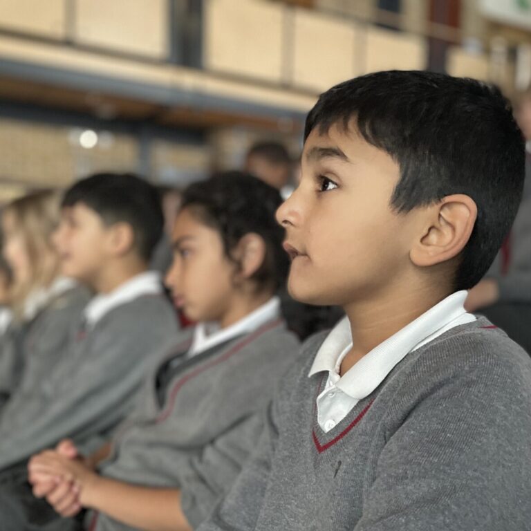 Junior pupils watching a performance in the theatre. They are sitting in red seats and looking at the stage
