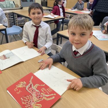 Two schoolboys in the Art studio, with gold-painted fire horses, drawn on red paper, to celebrate Lunar New Year
