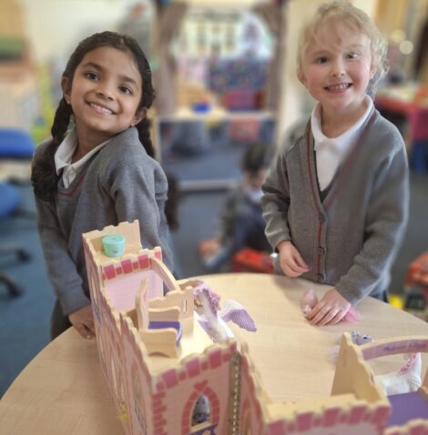 Two girls in front of a pink fairy castle toy, both smiling at the camera