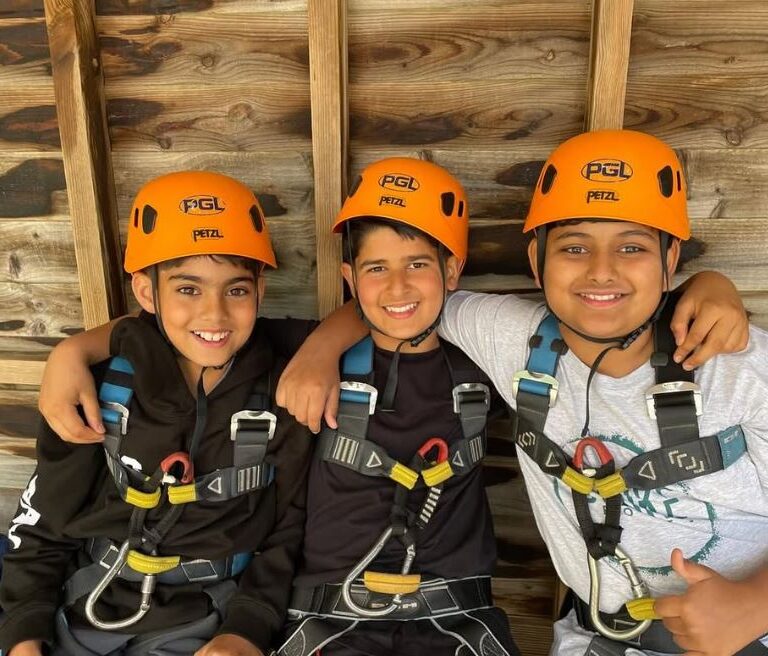 Three smiling children wearing orange helmets before climbing the wall